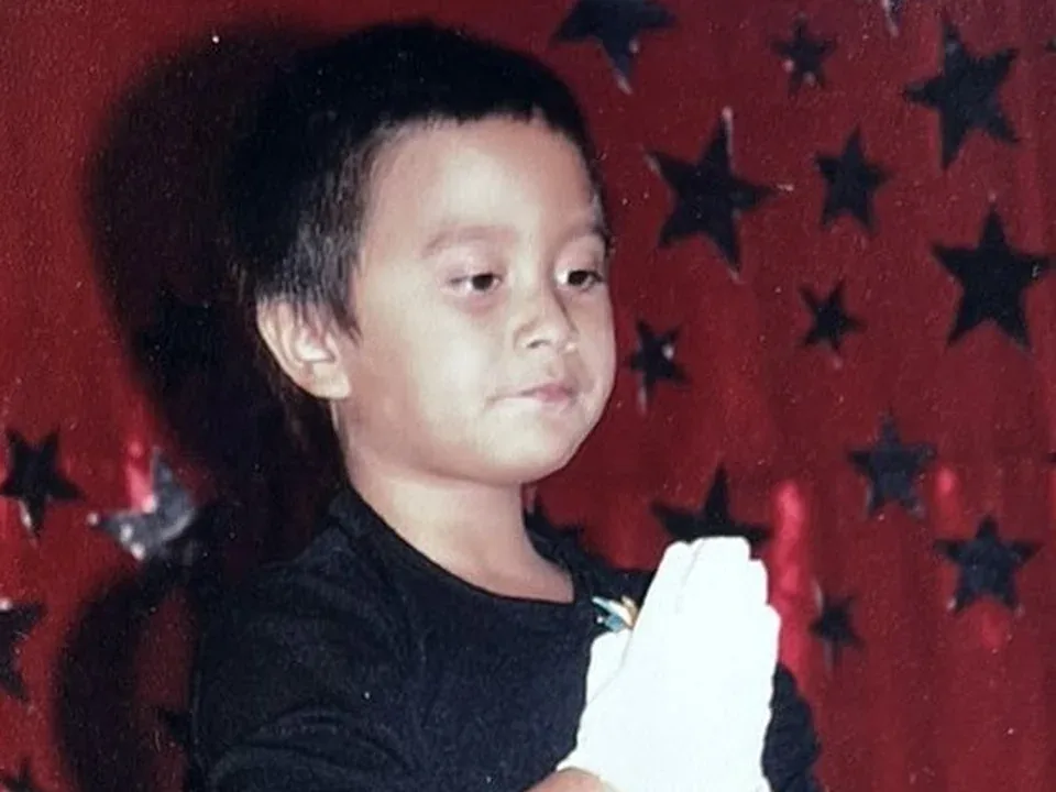 Cole as a child in a black costume on a stage with stars behind him